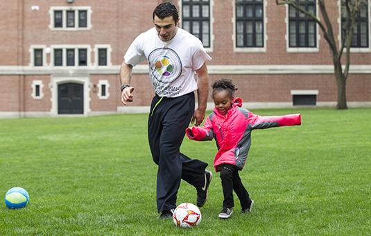 Student playing soccer with chil